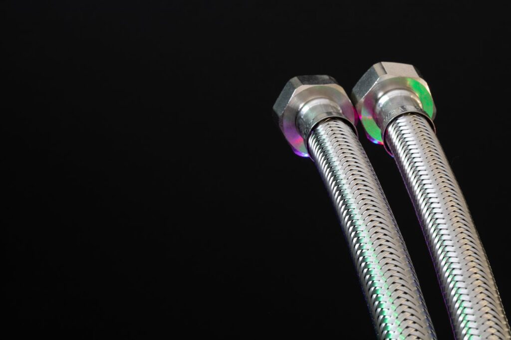 Close-up of metal flex pipes with hex nuts on a black background, showcasing industrial design.