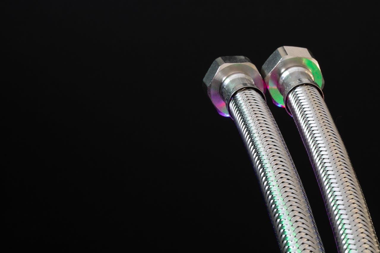 Close-up of metal flex pipes with hex nuts on a black background, showcasing industrial design.