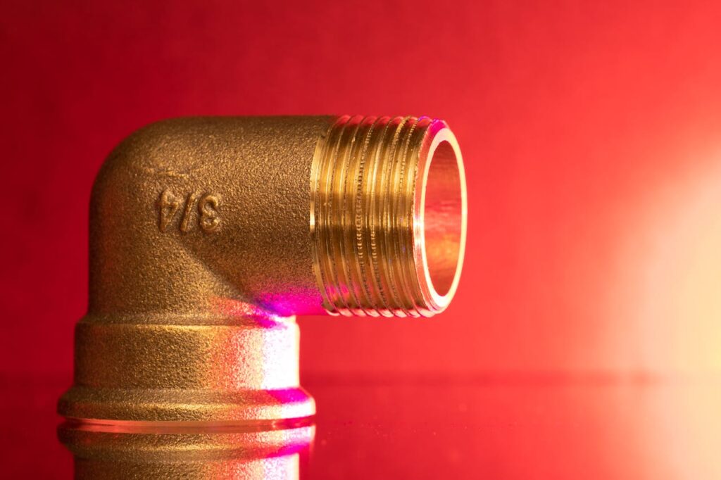 pexels-photo-28178448 Close-up of a shiny brass pipe elbow fitting against a vibrant red backdrop, showcasing industrial elegance.